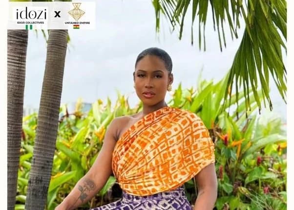 A woman is seen wearing a traditional Ghanaian dress. The dress is orange, white, and purple in color and appears to be made of cotton. The photograph could be related to fashion and cultural events in Accra.