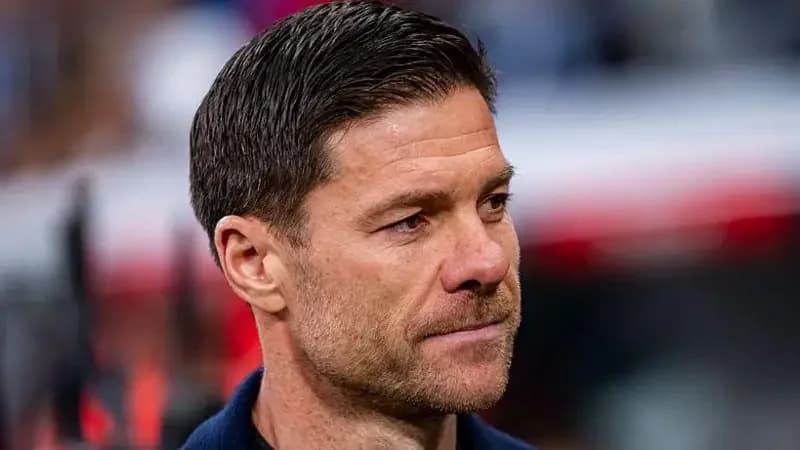 A high-quality, close-up photograph of football manager Xabi Alonso looking thoughtful and serious. He is captured from a side profile against a shallow depth-of-field background, emphasizing his facial expression within a stadium environment.