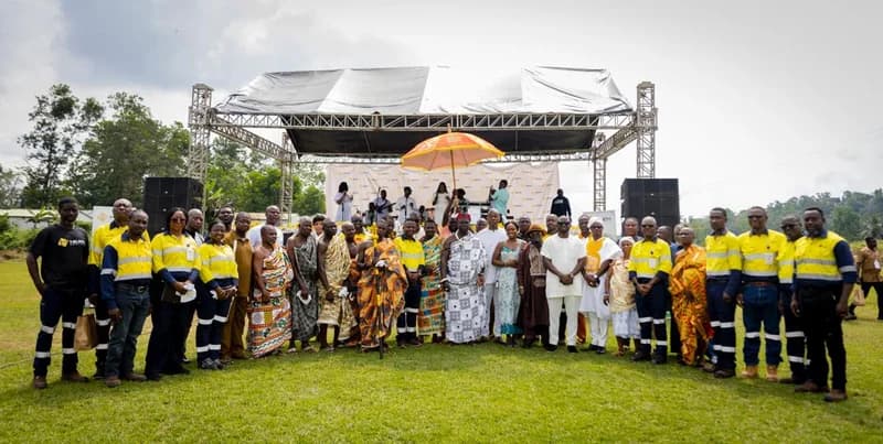 A group photograph featuring traditional Ghanaian chiefs in ceremonial Kente cloth and Heath Goldfields employees in yellow high-visibility uniforms. They are gathered outdoors in front of a covered stage during a community engagement event for the Bogoso-Prestea Mine.