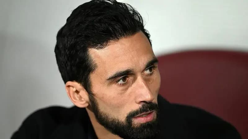 This is a headshot of a man with dark hair and a beard. He is wearing a dark jacket and looking off to the side. The image appears to be a professionally taken photograph.