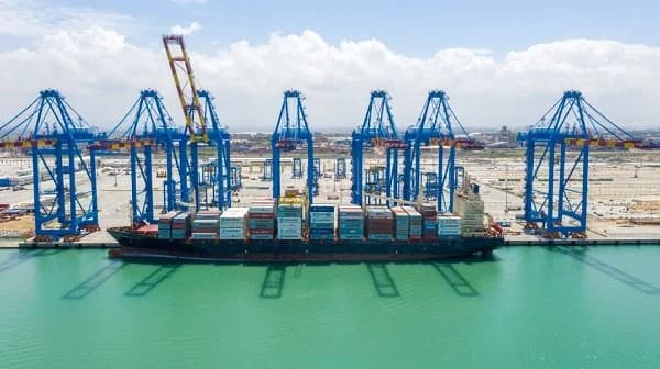 The image shows a large cargo ship docked at a port, likely in Ghana, surrounded by numerous gantry cranes used for loading and unloading containers. The port appears busy, indicating active shipping and trade operations. This aligns with the article's focus on the Ghana Shippers Authority and Smart Port Notes.