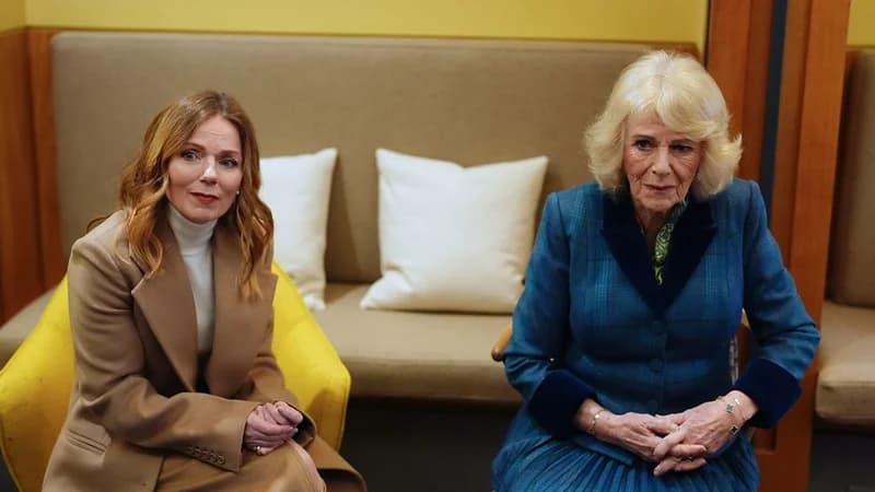 The image shows Queen Camilla and Geri Halliwell (Ginger Spice of the Spice Girls) seated side-by-side. They appear to be in a reception area, possibly at the cancer center mentioned in the related article. Both women are formally dressed and appear to be engaged in conversation.