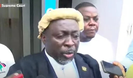 Ghanaian politician and lawyer Baba Jamal is pictured wearing a legal wig and gown while addressing the press. He is surrounded by microphones and smartphones, indicating a media briefing likely occurring at a court premises.
