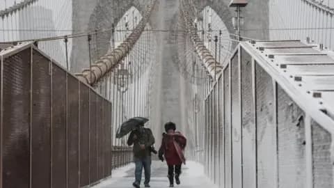 Reuters People walk across the Brooklyn Bridge as snow falls during a winter storm in New York Cit on 22 February 2026.