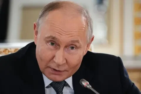 EPA Putin dressed in a dark blue suit, light blue shirt and spotted tie leans into a microphone, his eyebrows raised, at a press conference