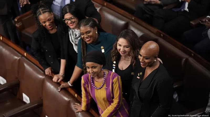 A group of diverse female politicians, including US Representatives Ilhan Omar and Ayanna Pressley, are seen posing together in a legislative chamber. The image highlights women's representation in high-level governance and political leadership roles.