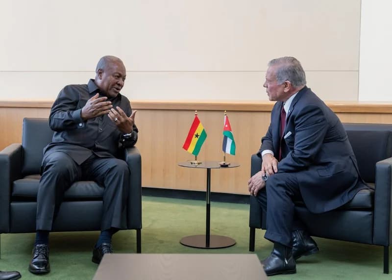 President John Mahama of Ghana and King Abdullah II of Jordan are pictured in a formal diplomatic meeting. The two leaders are seated in black leather armchairs, engaged in conversation with the flags of Ghana and Jordan positioned on a table between them.