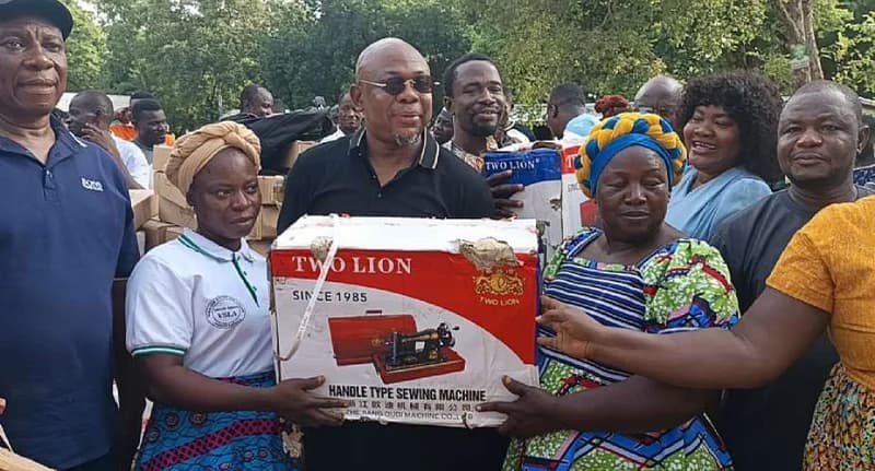 Member of Parliament for Builsa North, James Agalga, is seen presenting a 'Two Lion' brand sewing machine to community members during a donation event. He is surrounded by local residents and apprentices in an outdoor setting, marking a significant empowerment initiative in his constituency.