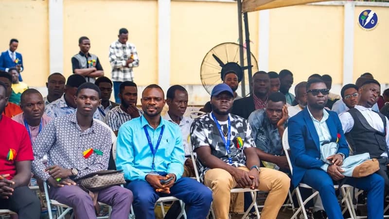 A large group of men, primarily young professionals, are seated in rows of white chairs at what appears to be an outdoor certification or graduation ceremony. Many attendees are wearing lanyards with identification badges, and the official Energy Commission logo is visible in the top right corner of the frame.