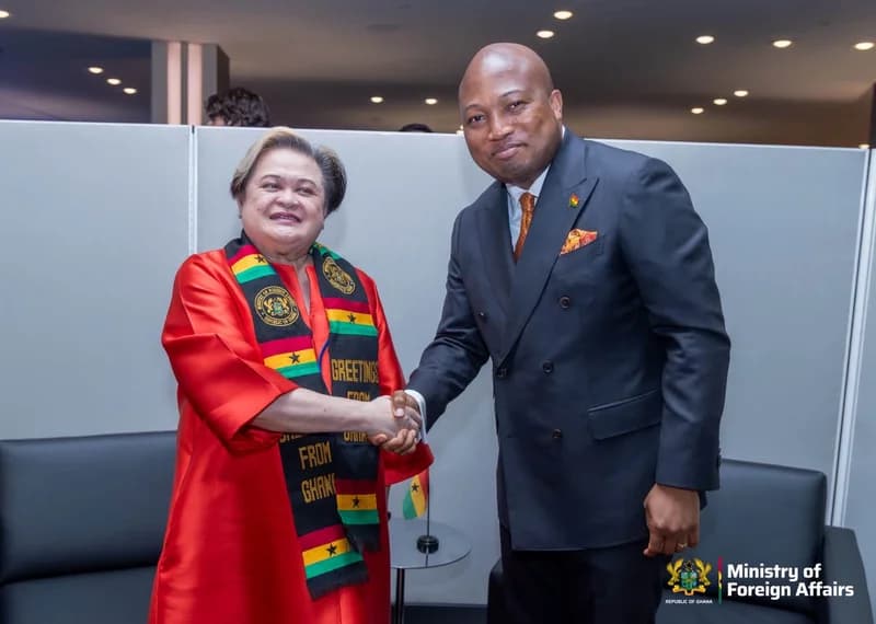A photograph of Ghanaian Member of Parliament Samuel Okudzeto Ablakwa shaking hands with a female official from the Philippines. The official is dressed in a red ensemble and wears a scarf featuring the colors of the Ghana flag and the text 'Greetings from Ghana', symbolizing diplomatic cooperation between the two nations.