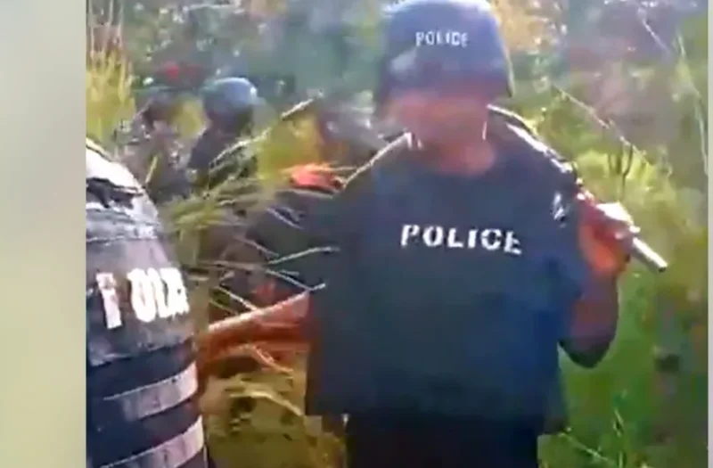 A low-resolution image showing several police officers in tactical gear, including helmets and vests marked with 'POLICE', conducting an operation in a forested area. The scene appears to be a field investigation or search mission in a rural, wooded environment.