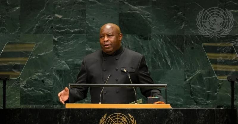 President Évariste Ndayishimiye of Burundi is seen delivering a speech from a podium at the United Nations. He is wearing a dark, high-collared suit and stands before a distinctive green marble backdrop featuring the UN logo.