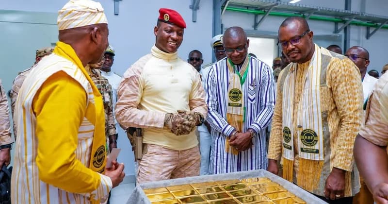 Captain Ibrahim Traore, Burkina Faso's junta leader, is pictured in military fatigues and a red beret alongside officials at the opening of a new gold refinery. They are gathered around a display of processed gold bars, signifying the country's move to refine its mineral resources domestically.