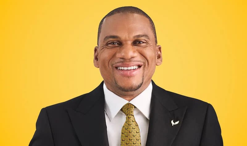 A professional portrait of Kofi Adomakoh, Managing Director of GCB Bank PLC, smiling against a vibrant yellow background. He is wearing a dark suit, a white shirt, and a gold-patterned necktie with a small GCB eagle logo pin on his lapel.