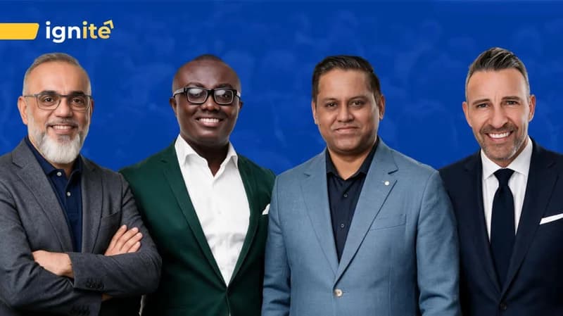 Four professionally dressed men are posed side-by-side against a solid blue background that features the word 'ignite' and an upward arrow logo in the top left corner. The group includes diverse individuals in business attire, including a Black man in a green blazer, suggesting a professional or technology-themed conference setting.