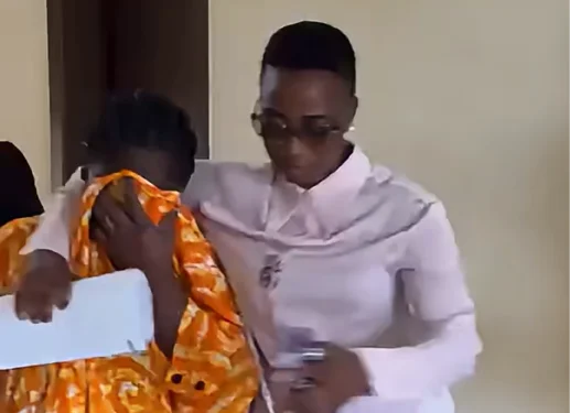 A woman in a bright orange and white patterned outfit covers her face as she is escorted by another woman in a light shirt and glasses. The scene likely depicts the accused, Salomey Awiti Baffoe, leaving court after being granted bail in the 'Ghana Jollof' case.