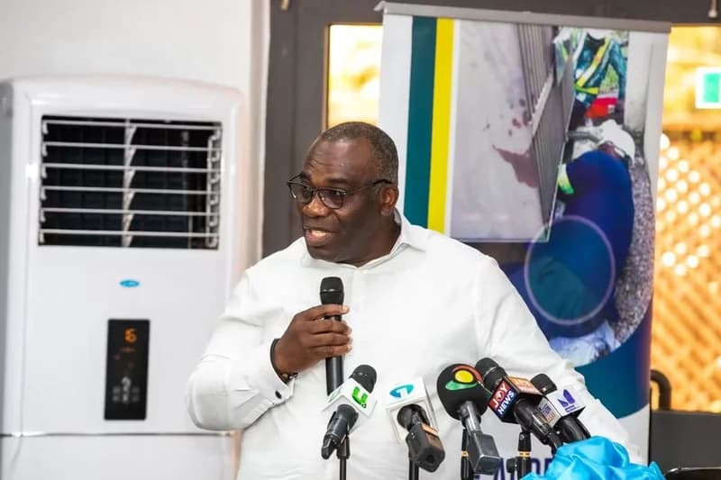 A man in a white shirt and glasses, identified as Emmanuel Antwi-Darkwa, CEO of the Volta River Authority (VRA), addresses the media during a press conference. He is speaking into a microphone with several other media house microphones, including Joy News and GTV, positioned in front of him.