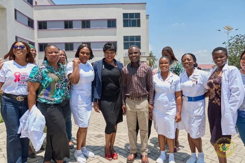 A group of Ghanaian health professionals and officials posing for a photograph in front of a multi-story medical facility. The group includes nurses in white uniforms and individuals in formal attire, representing a collaborative gathering within the healthcare sector under the Ministry of Health.