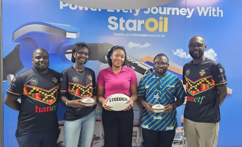Five individuals, including representatives from StarOil and the Rugby League Federation Ghana, stand together for a group photo in front of a branded backdrop. Three of the individuals are wearing official black and kente-patterned jerseys while holding rugby balls, highlighting a corporate sponsorship deal.