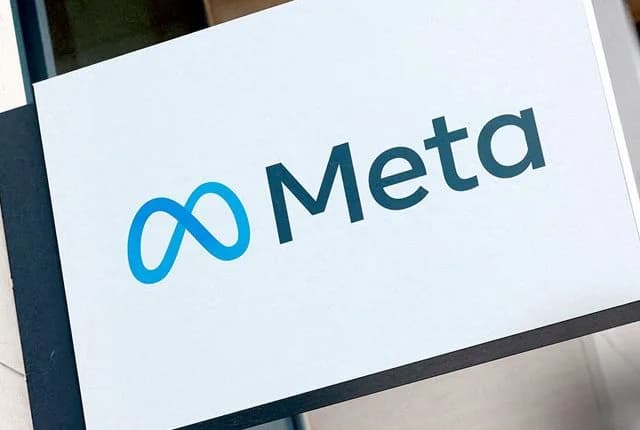 A close-up photograph of a corporate sign featuring the Meta logo and name. The blue infinity symbol is positioned to the left of the word 'Meta' in a dark teal font against a clean white background.