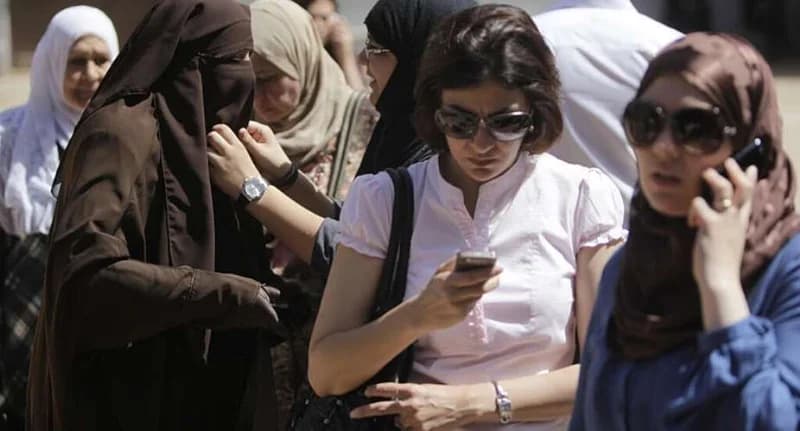 A group of Egyptian women are seen in a public space, illustrating a mix of traditional and modern attire. Several women are actively using smartphones, which connects to the news story about how mobile technology and femtech are being used to address women's health in Egypt.