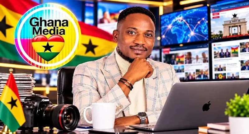 A media professional in a checkered blazer sits at a desk in a modern studio, posing with his hand on his chin. The workspace includes a laptop, a high-end DSLR camera, and a mug, while background screens display Ghanaian news elements and a prominent 'Ghana Media' logo. This setting reflects the modernization and digital shift of Ghanaian journalism.