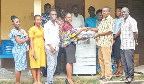 Salomey Appiah Adjei (4th from left), Operations Manager of the foundation, handing over the learning materials to Harrison Mompi (2nd from right), headmaster of the school