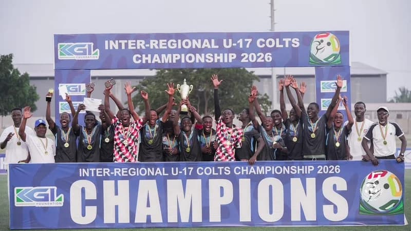 A joyous group of young footballers from the Greater Accra regional team celebrates winning the KGL Inter-Regional U-17 Colts Championship 2026. The players are seen cheering and holding a trophy on a victory podium decorated with banners acknowledging them as champions.