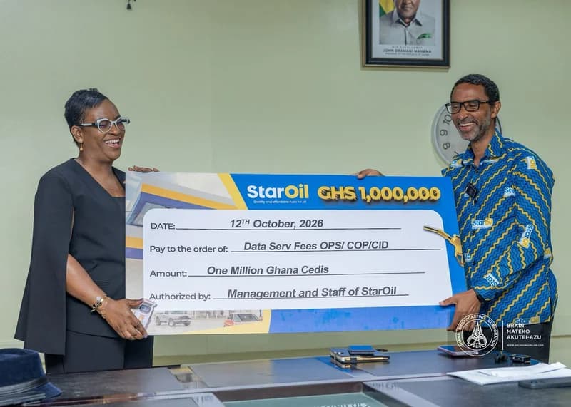 A man and a woman smile as they present a large ceremonial check for GH¢ 1,000,000 from Star Oil, donated to the CID. The man wears a blue Star Oil branded shirt, and a portrait of President John Dramani Mahama is visible on the office wall in the background.