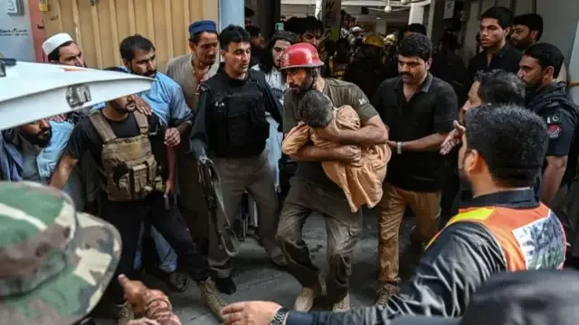 An emergency service worker carrying a child out of a school in Pakistan as other emergency workers line the corridors