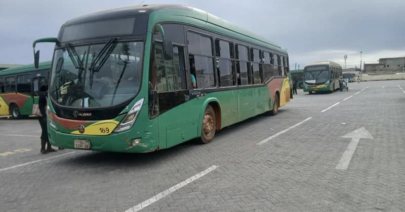 The image displays several green and gold Aayalolo BRT buses parked in a paved transit terminal under a cloudy sky. The foreground focuses on a green bus with registration number GS 5197-18 and vehicle number 169, while other buses and transit workers are visible in the background.