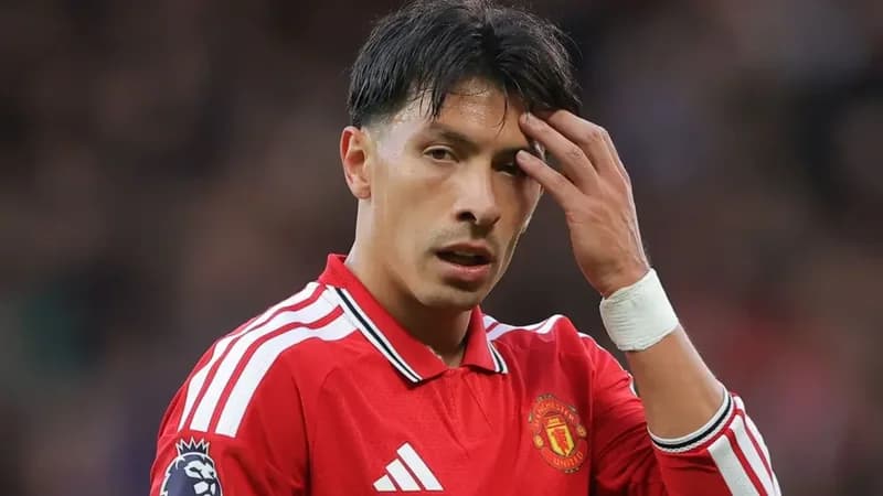A close-up photograph of Manchester United player Lisandro Martínez looking frustrated or concerned during a match. He is wearing the red club home kit and has his left hand raised to his head, appearing stressed.