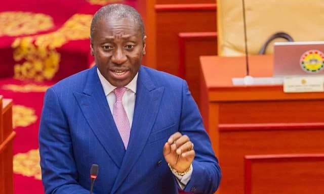 Alexander Kwamena Afenyo-Markin, a prominent Ghanaian politician, is captured speaking in Parliament. He is dressed in a blue suit and a pink tie, gesturing with his hand while addressing his colleagues.