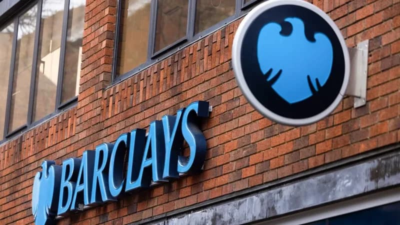 A photograph of the exterior of a Barclays bank building featuring the prominent blue corporate branding against a red brick facade. The image displays the word 'BARCLAYS' in large blue letters alongside the company's eagle logo on a circular sign.