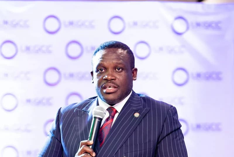 Hon. Sam Nartey George, MP for Ningo-Prampram, is captured delivering a speech while holding a microphone. He is dressed in a formal pinstriped suit and stands before a branded backdrop, likely at a technology-related forum or government announcement.
