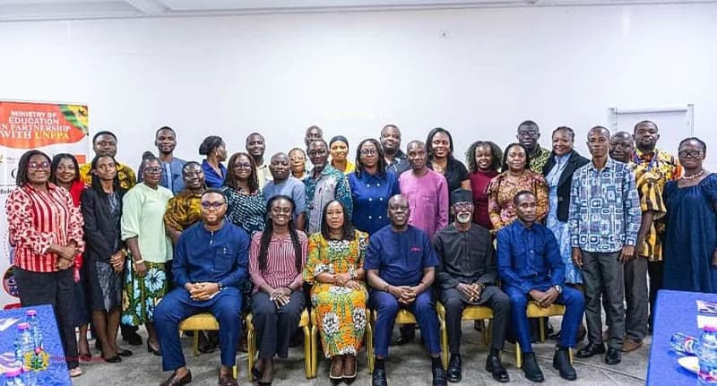 A large group of representatives from Ghana's Ministry of Education and the United Nations Population Fund (UNFPA) pose for a collective photograph during a partnership event. The image shows approximately thirty-three participants, with key officials seated in the front row and others standing behind them against a plain white wall. A banner on the left clearly displays the collaboration between the ministry and the international organization.