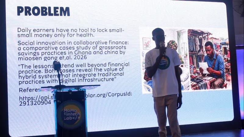 A young man stands on a stage presenting a pitch during the MoMo FinTech Lab event. Behind him, a large screen displays a slide titled 'PROBLEM' that discusses financial tools for daily earners, while the podium features the MoMo Fintech Lab branding.