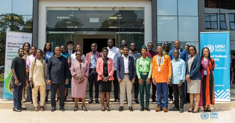 A group of approximately 22 professionals pose for a group photo in front of a modern glass building. Flanking the group are two vertical banners, one identifying the event as the 'African Technical Workshop on the Global Goal on Adaptation Indicators' and the other featuring the UNU-INRA logo.