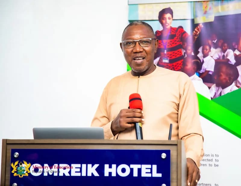 Dr. Clement Apaak, the Member of Parliament for Builsa South, is pictured speaking at a podium at the Omreik Hotel. He is holding a microphone and standing in front of a Ministry of Education banner featuring a teacher and students in a classroom.