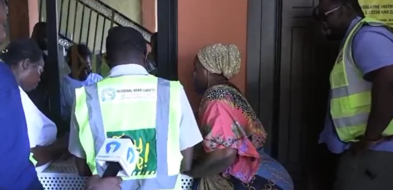 Officials in high-visibility vests are seen conducting an enforcement exercise at a building entrance, likely an unlicensed Airbnb facility in Kasoa. A news microphone with a '7' logo is present, indicating media coverage of the Ghana Tourism Authority's crackdown on unauthorized hospitality services.