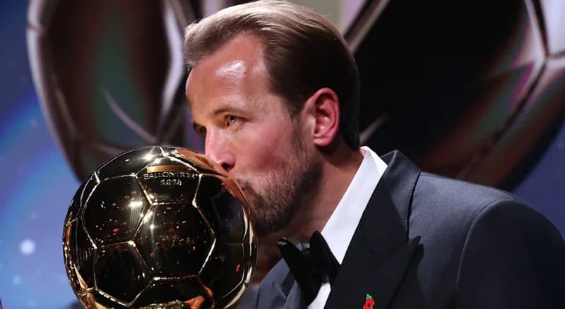 England captain Harry Kane is pictured kissing the Ballon d'Or trophy during the 2024 award ceremony. He is dressed in a formal black tuxedo with a bow tie and a commemorative poppy pin, celebrating his historic achievement.
