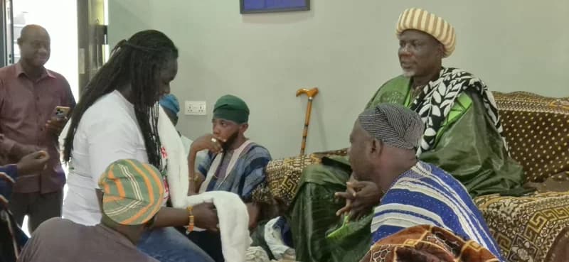 The image shows a ceremony at a traditional palace in Tamale where a woman, likely the EPA CEO, is being honored. She stands before a traditional ruler dressed in a rich green and white robe, while others in the room wear traditional Northern Ghanaian smocks. The scene captures a formal exchange between government officials and traditional leadership.