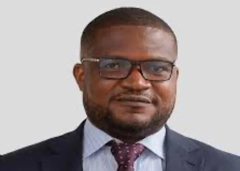 A head-and-shoulders portrait of Martin Ayisi, CEO of the Minerals Commission of Ghana. He is wearing a dark navy suit jacket, a light blue shirt, a dotted maroon tie, and rectangular glasses against a plain light grey background.