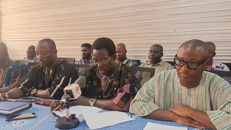 A group of men, identified as representatives of the Technical University Teachers' Association of Ghana (TUTAG), are seated at a press briefing. The central figure is reading from a prepared statement into a microphone, likely announcing the suspension of the union's industrial strike action.