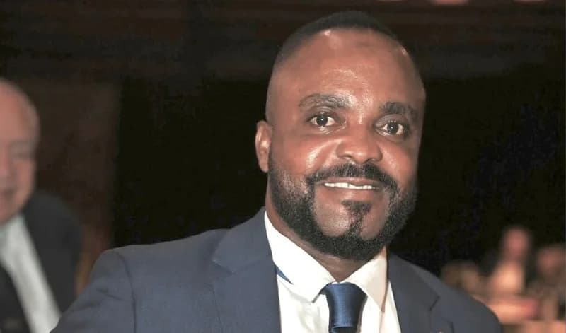 A headshot portrait of Abdul Yartey, President of the Ghana Bodybuilding and Fitness Association (GBFA). He is seen smiling while wearing a formal dark blue suit, a white dress shirt, and a matching navy blue necktie.